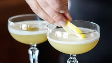 A hand squeezing a lemon into a cocktail glass.