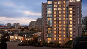 A modern hotel with a prominent Hilton logo, multiple floors, and a view of the surrounding cityscape. - Hilton Vancouver Airport (Richmond)
