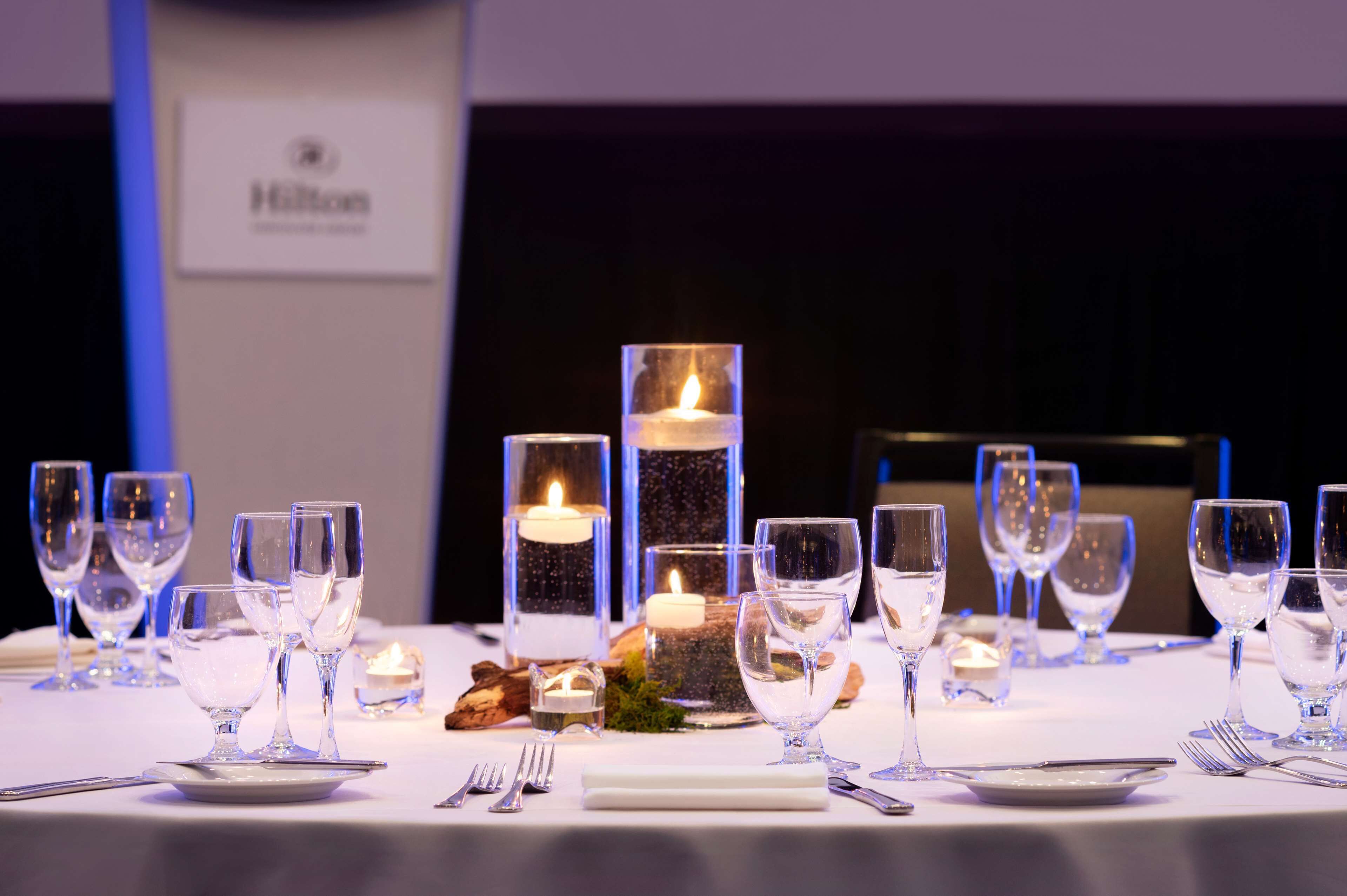 A table set for a formal dinner with clear glassware, candles, and a Hilton sign in the background.
