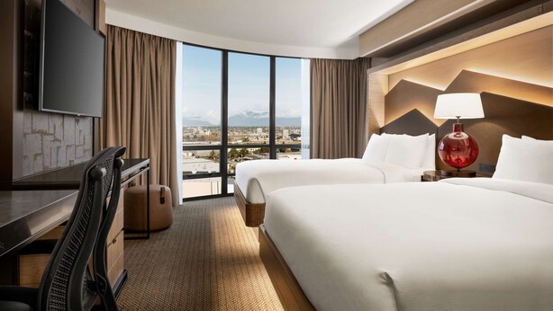 A hotel room with a large bed, a desk, a TV, and a view of the city. - Hilton Vancouver Airport (Richmond)