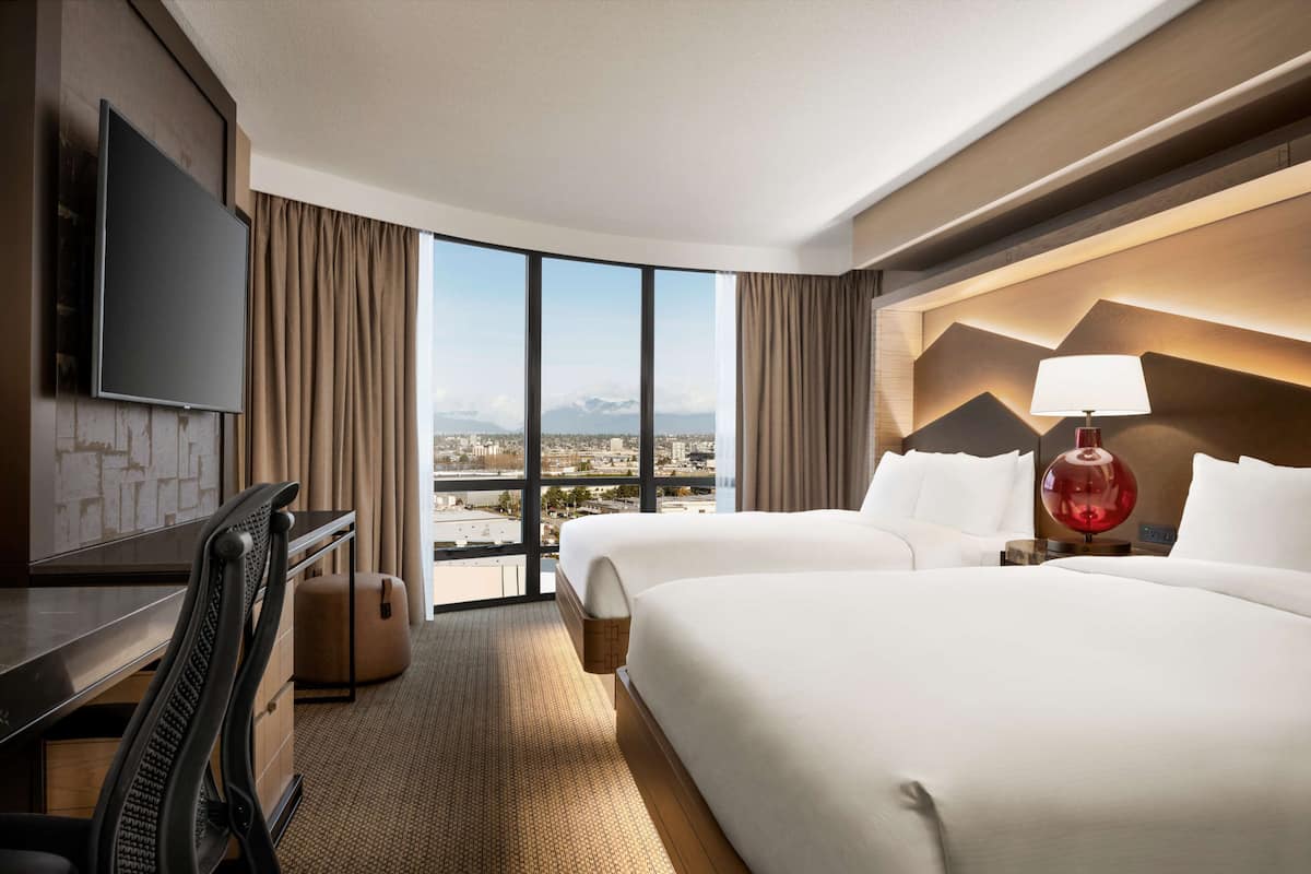 A hotel room with a large bed, a desk, a TV, and a view of the city.