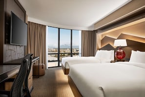 A hotel room with a large bed, a desk, a TV, and a view of the city. - Hilton Vancouver Airport (Richmond)