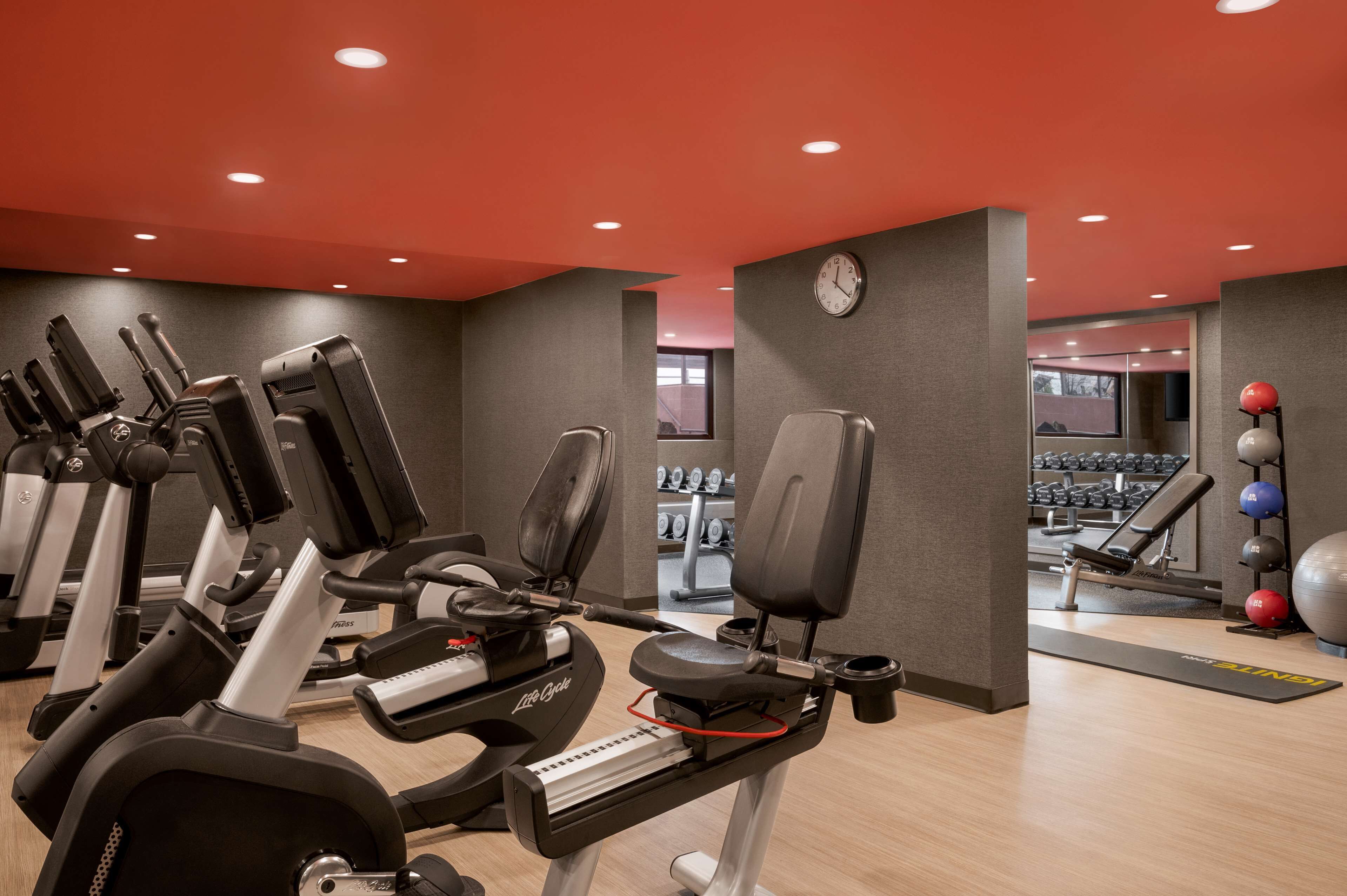 Une salle de sport équipée de plusieurs appareils de cardio, de matériel de musculation et d’une horloge au mur.