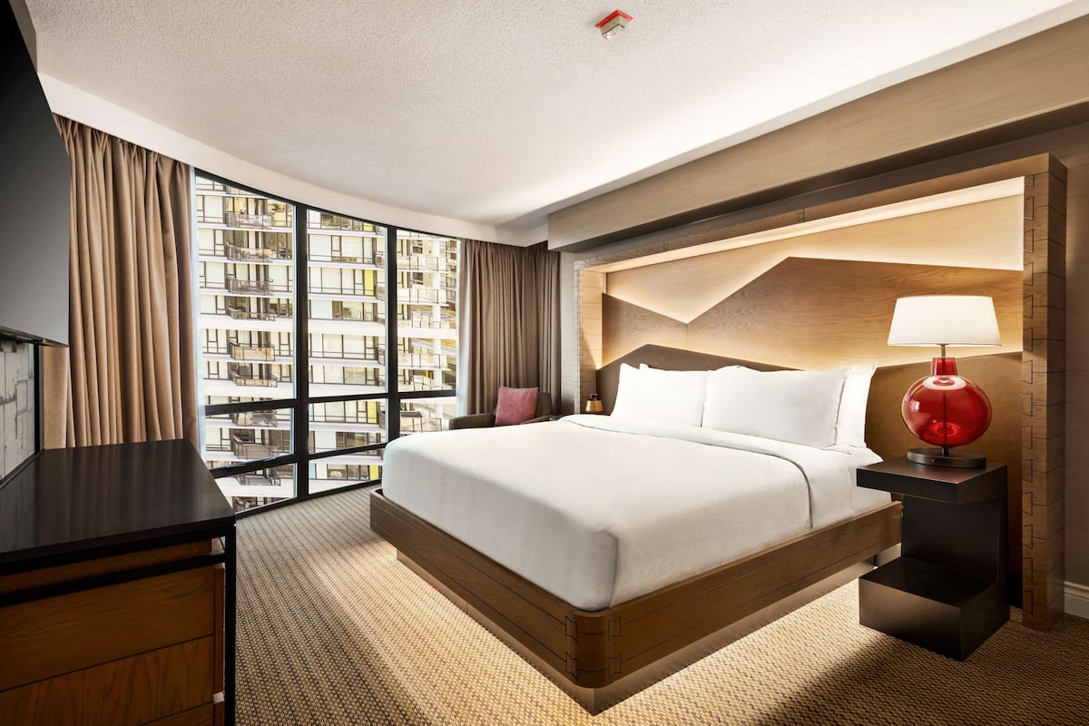 A hotel room with a large bed, a desk, a lamp, and a view of the city.
