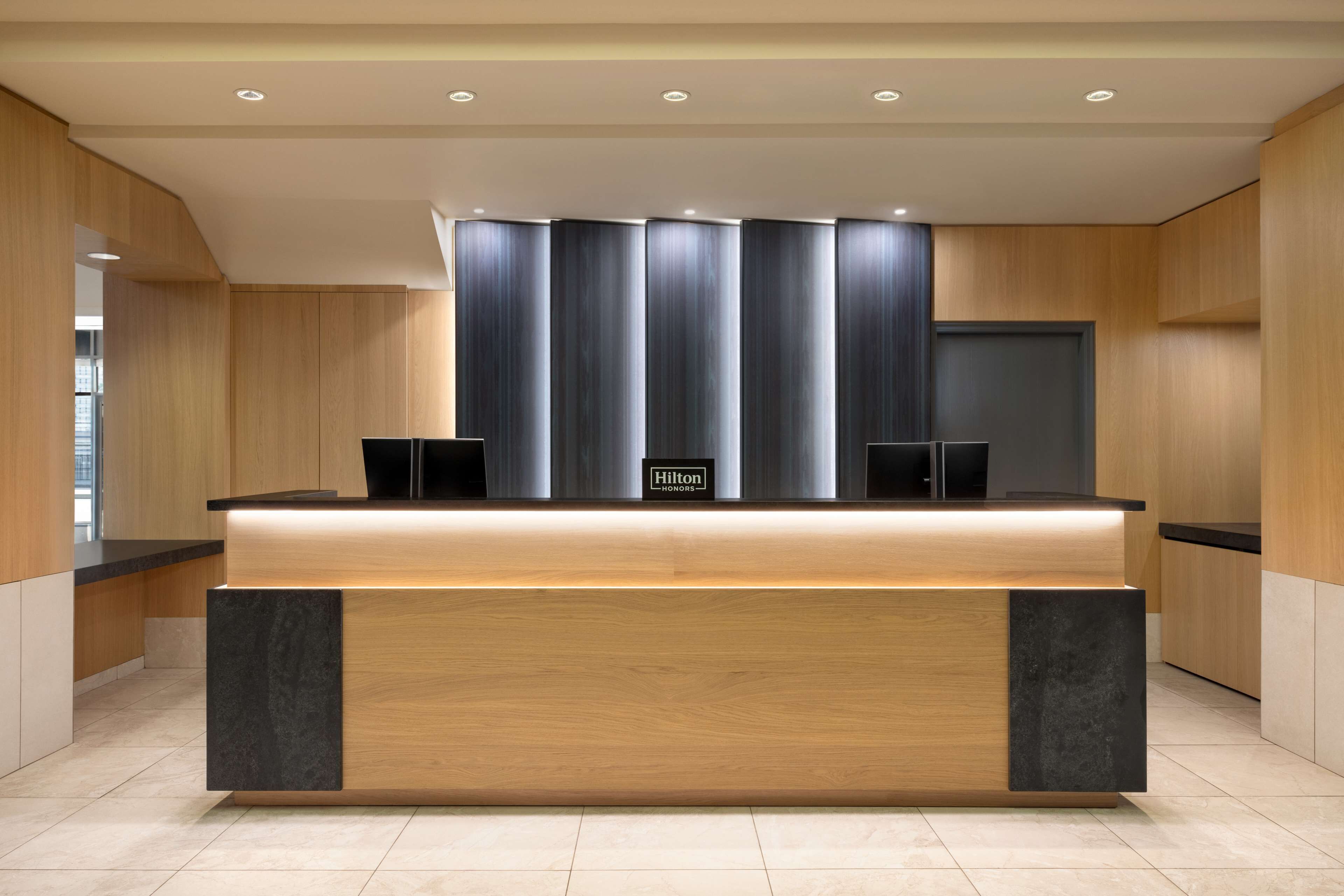 A modern hotel reception desk with a wooden finish and a black accent piece.