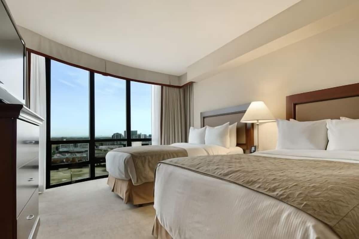 A hotel room with two beds, a city view, a large window, and a desk.