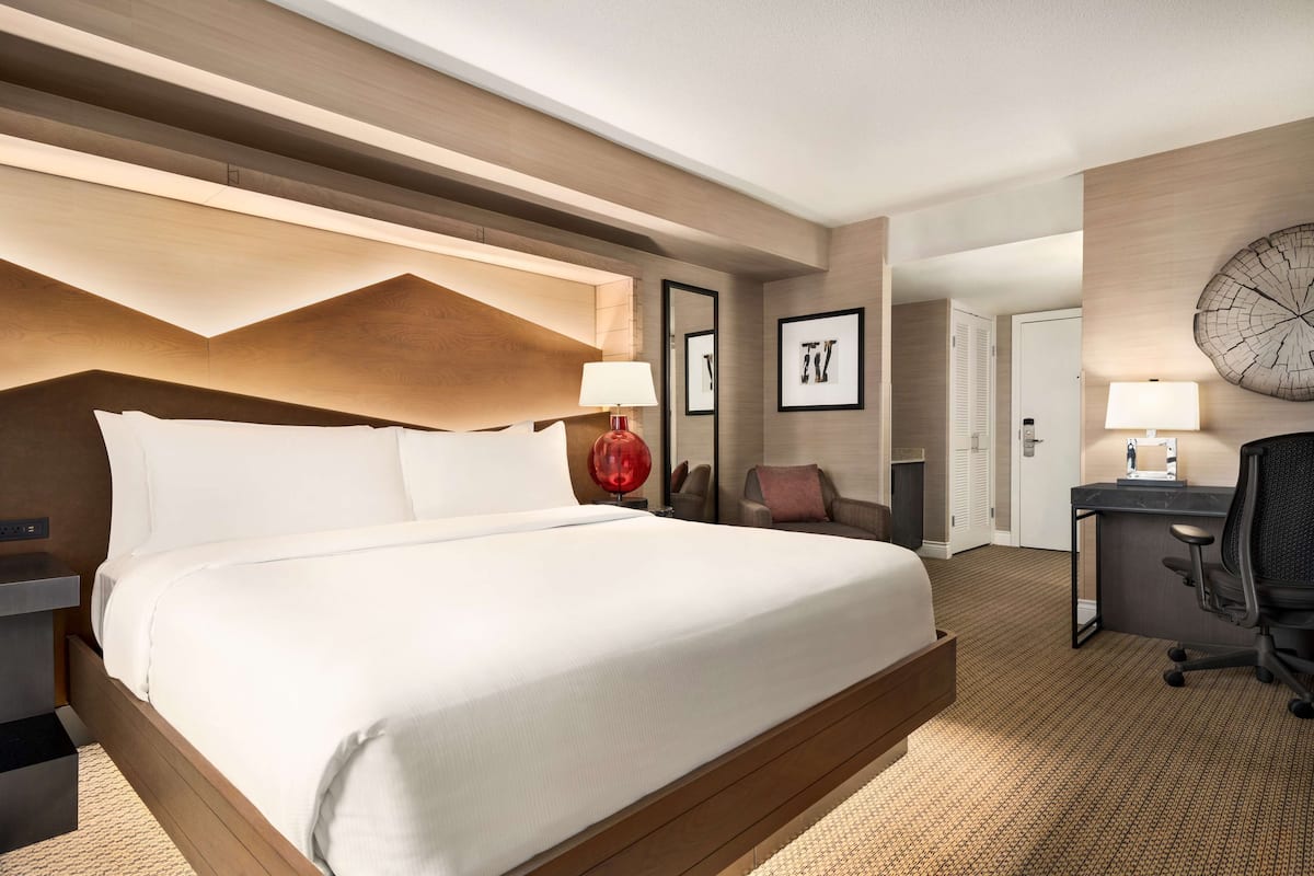 A hotel room with a large bed, a desk with a chair, a red lamp, and framed pictures on the wall.