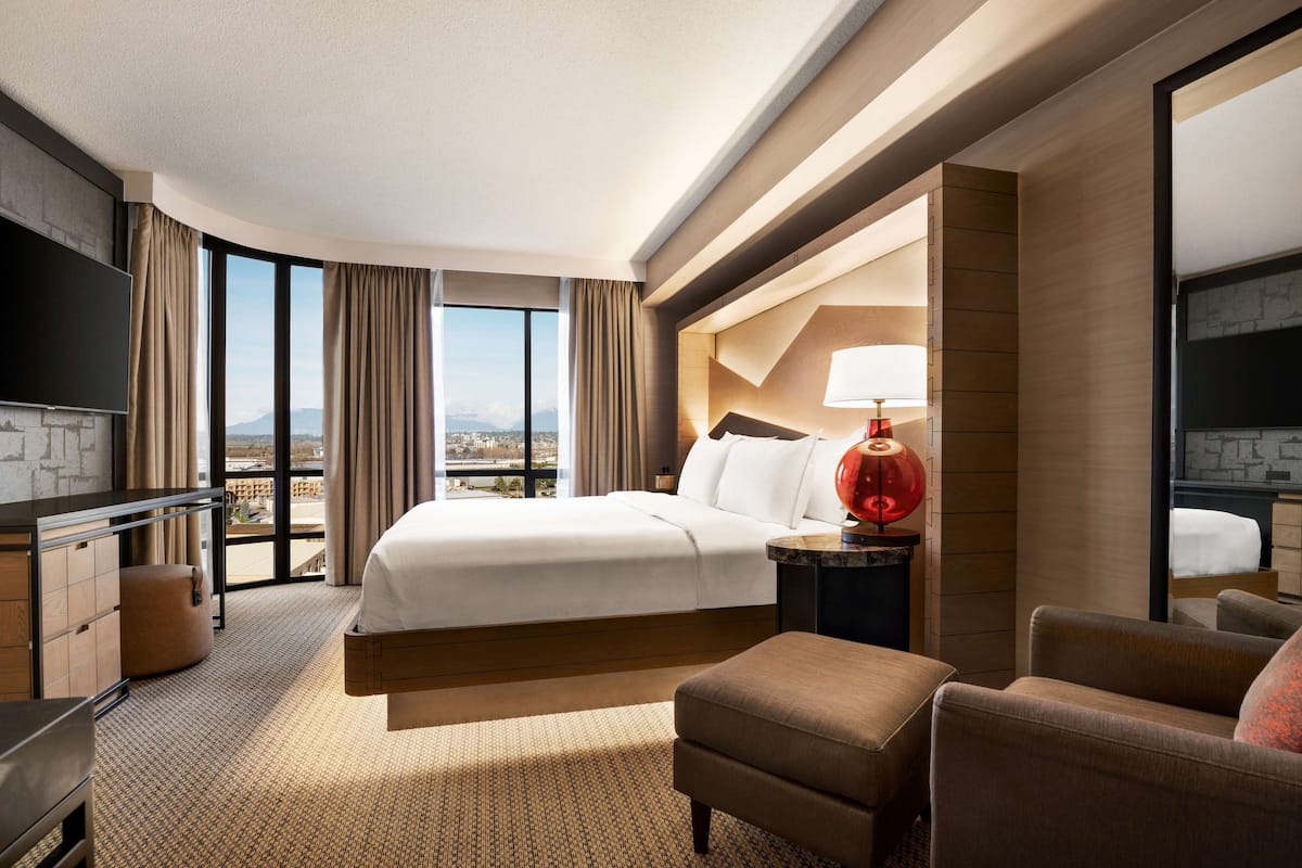 A hotel room with a large bed, a TV, a desk, and a view of the city.