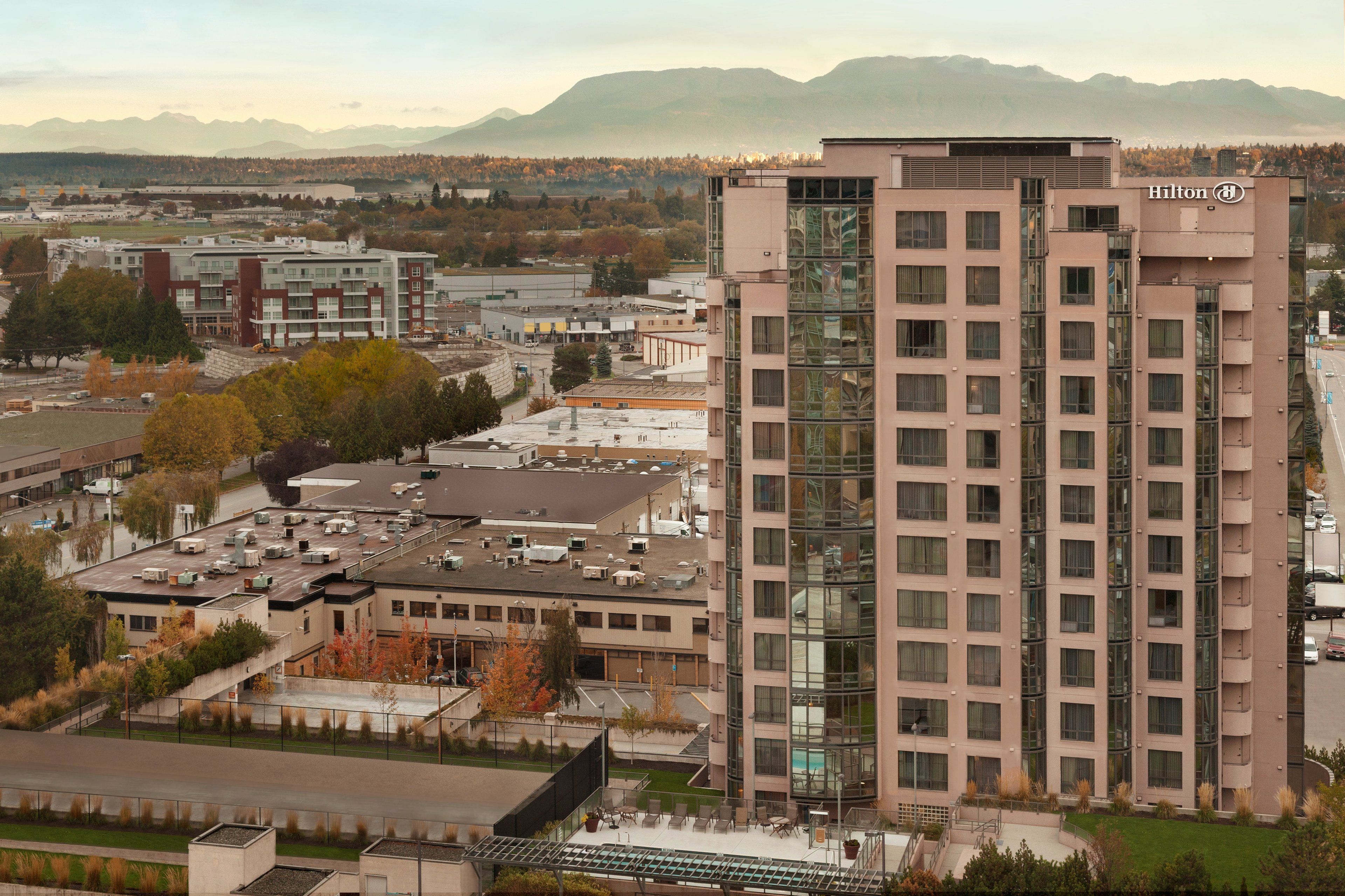 Ein modernes Hotel mit Glasfassade, mehreren Etagen und Blick auf umliegende Gebäude und Berge.