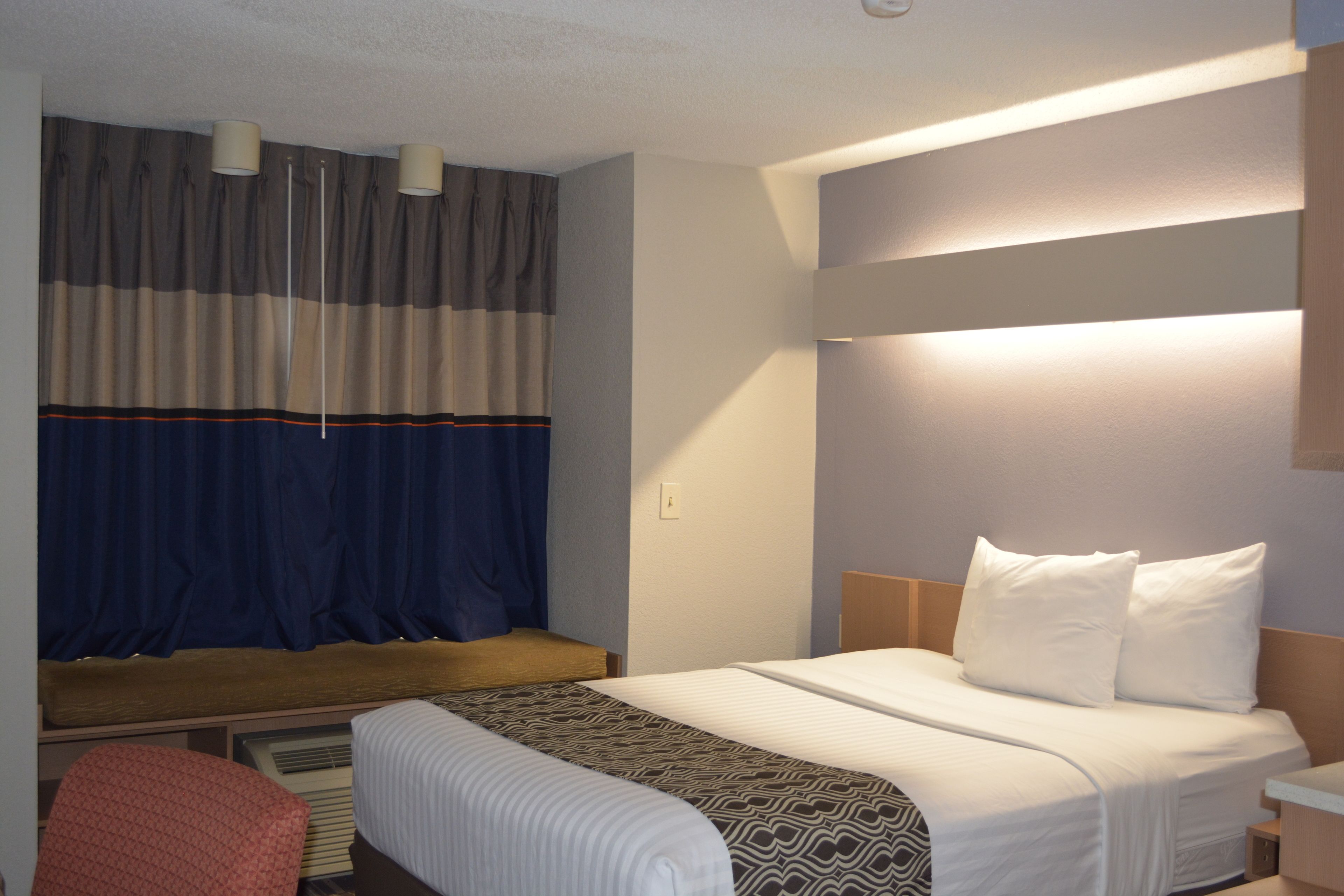 A hotel room with a bed, bedside table, lamp, and a window with curtains.