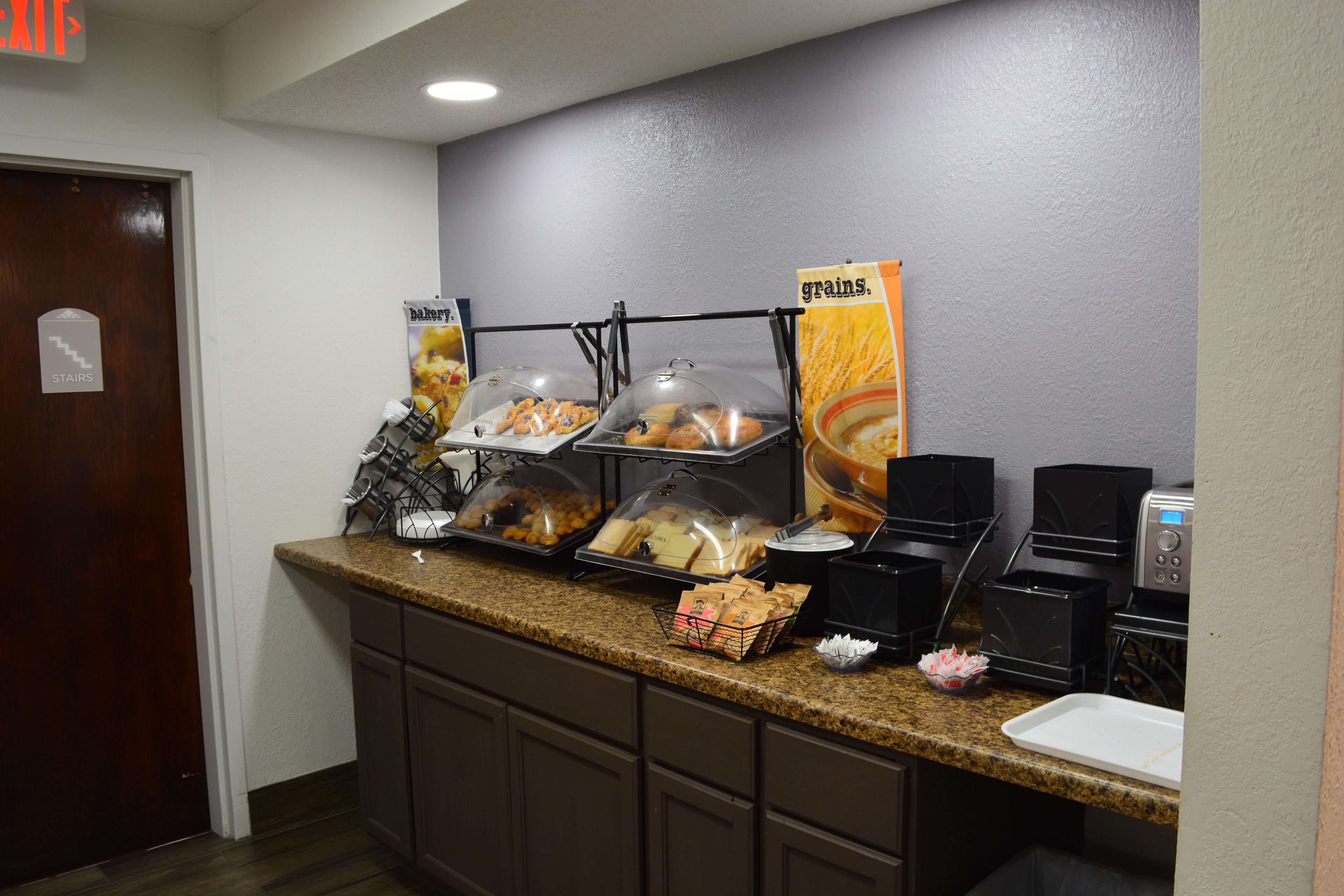 A breakfast bar with various food items, a coffee machine, and a sign indicating the exit.