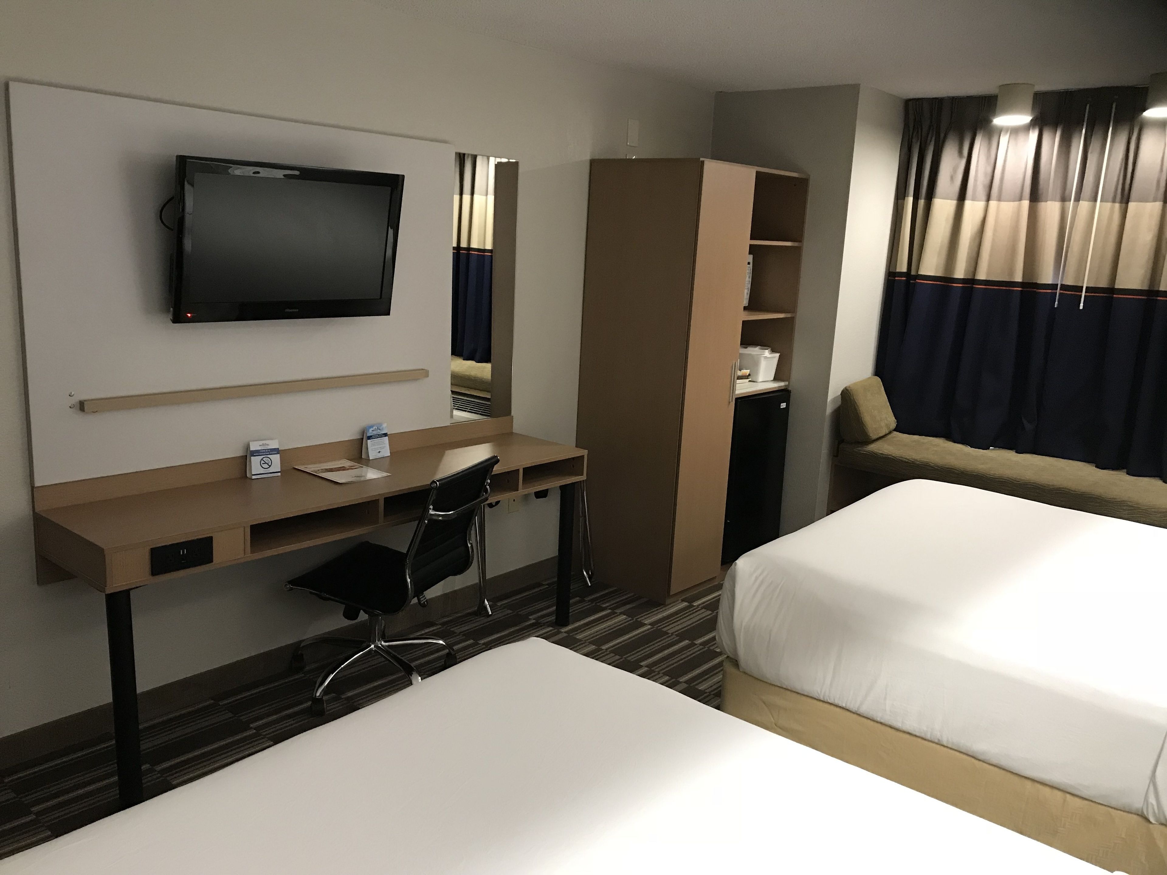 Habitació d'hotel amb un llit, una taula de treball amb una cadira, una televisió i un armari.