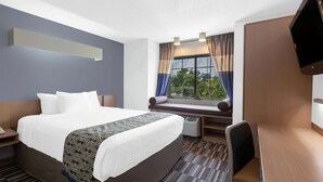 A hotel room with a large bed, a desk, a chair, a TV, and a window with curtains. - Microtel Inn & Suites by Wyndham Baltimore BWI Airport (Linthicum Heights)
