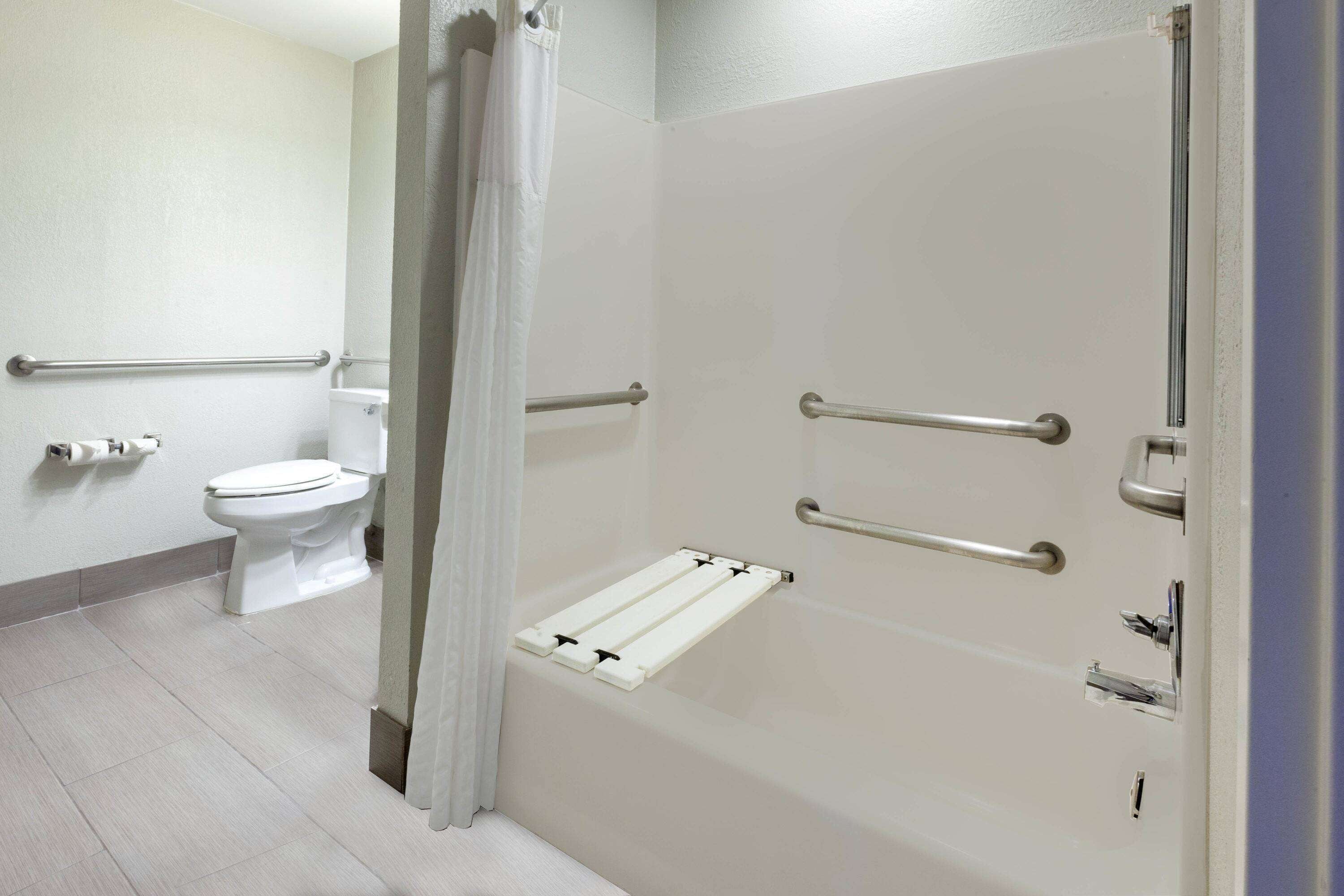 A bathroom with a shower, toilet, and grab bars.