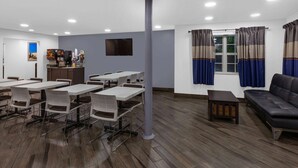 A conference room with tables and chairs, a sofa, a pillar, a television, and a window with curtains. - Microtel Inn & Suites by Wyndham Baltimore BWI Airport (Linthicum Heights)