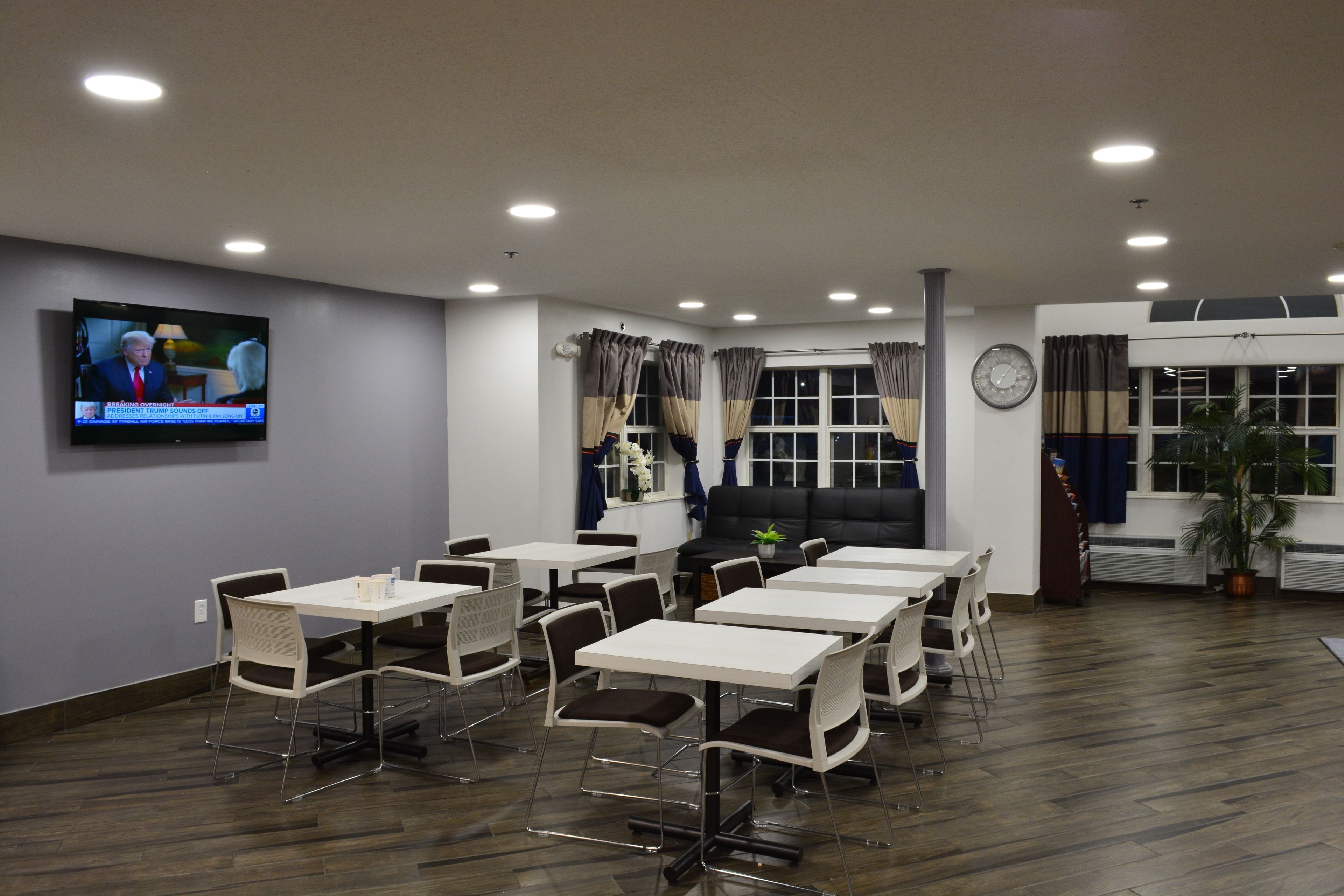 A conference room with tables and chairs, a television on the wall, and a clock.