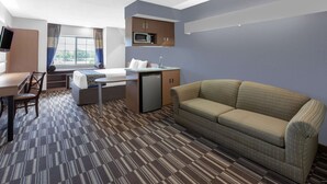 A hotel room with a bed, a sofa, a desk with a chair, a microwave, a sink, and a television. - Microtel Inn & Suites by Wyndham Baltimore BWI Airport (Linthicum Heights)