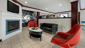A modern living room with a fireplace, a television mounted above it, a black leather sofa, a red armchair, and a round table with a bowl of fruit. - Best Western Edinburgh/Columbus (Edinburgh)