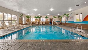 An indoor swimming pool with clear water, surrounded by lounge chairs and tables, and palm tree murals on the walls. - Best Western Edinburgh/Columbus (Edinburgh)