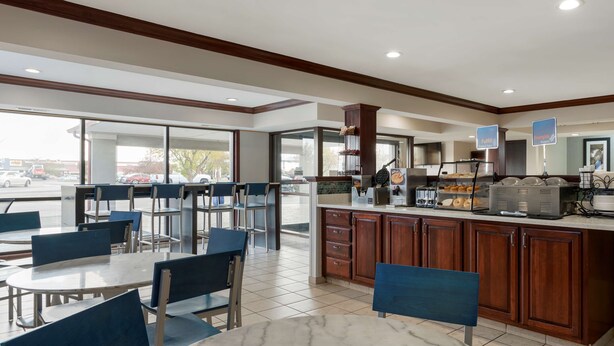 A hotel restaurant with marble-tiled tables and blue chairs, a kitchen area with a buffet, and large windows offering a view of the parking lot. - Best Western Edinburgh/Columbus (Edinburgh)
