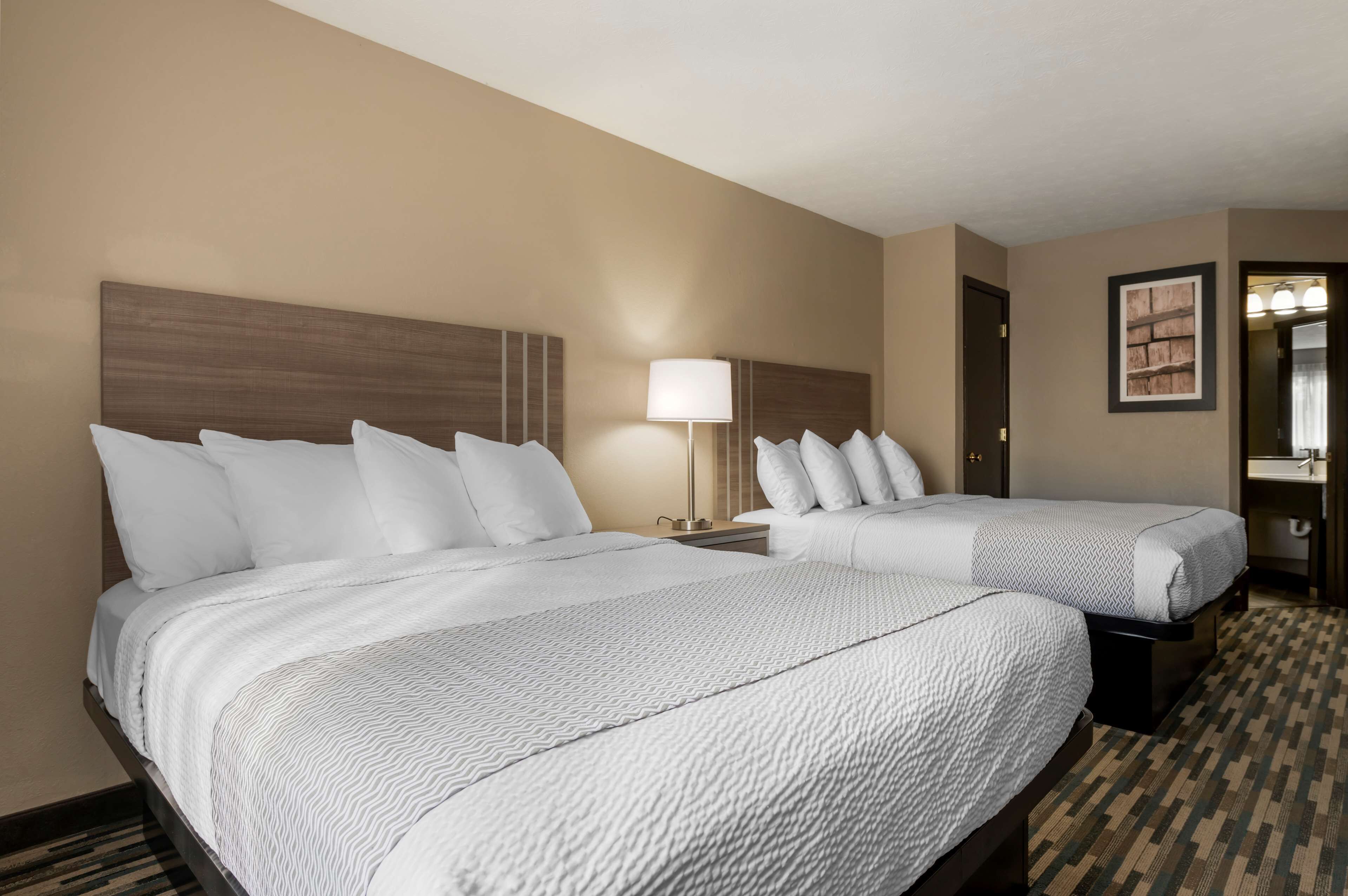 A hotel room with two beds, a nightstand with a lamp, a small table, and a framed picture on the wall.