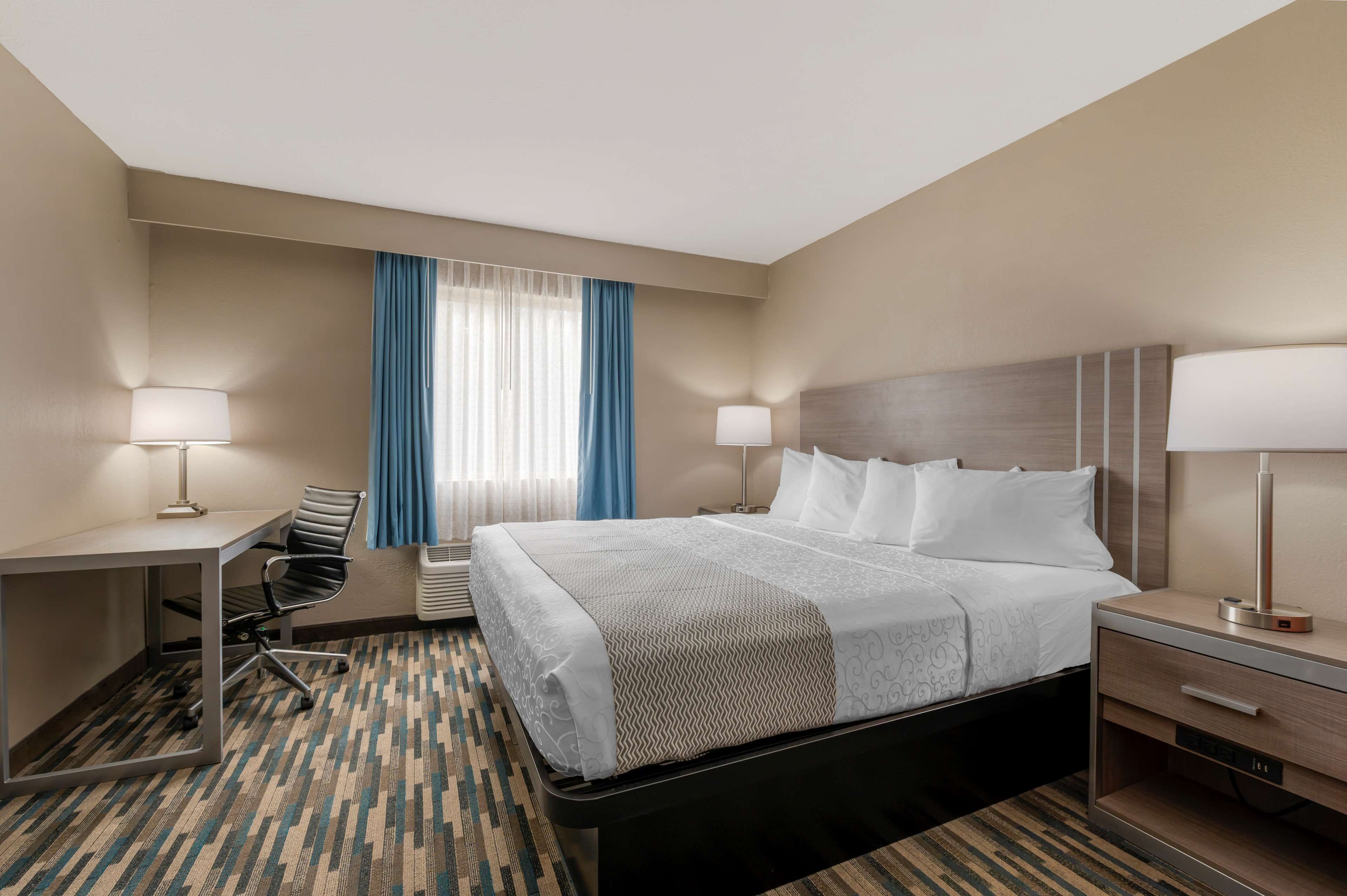 A hotel room with a bed, desk, chair, and bedside table.
