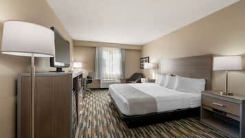A hotel room with a large bed, a desk with a chair, a television, and a window with curtains.