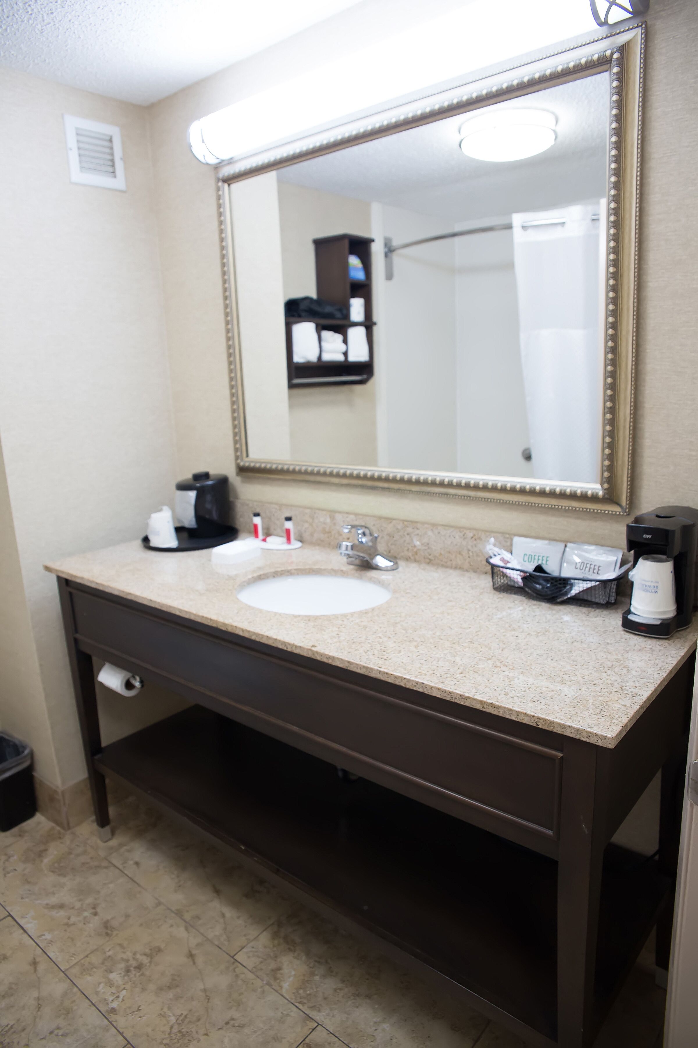 A bathroom with a sink, mirror, and coffee maker.