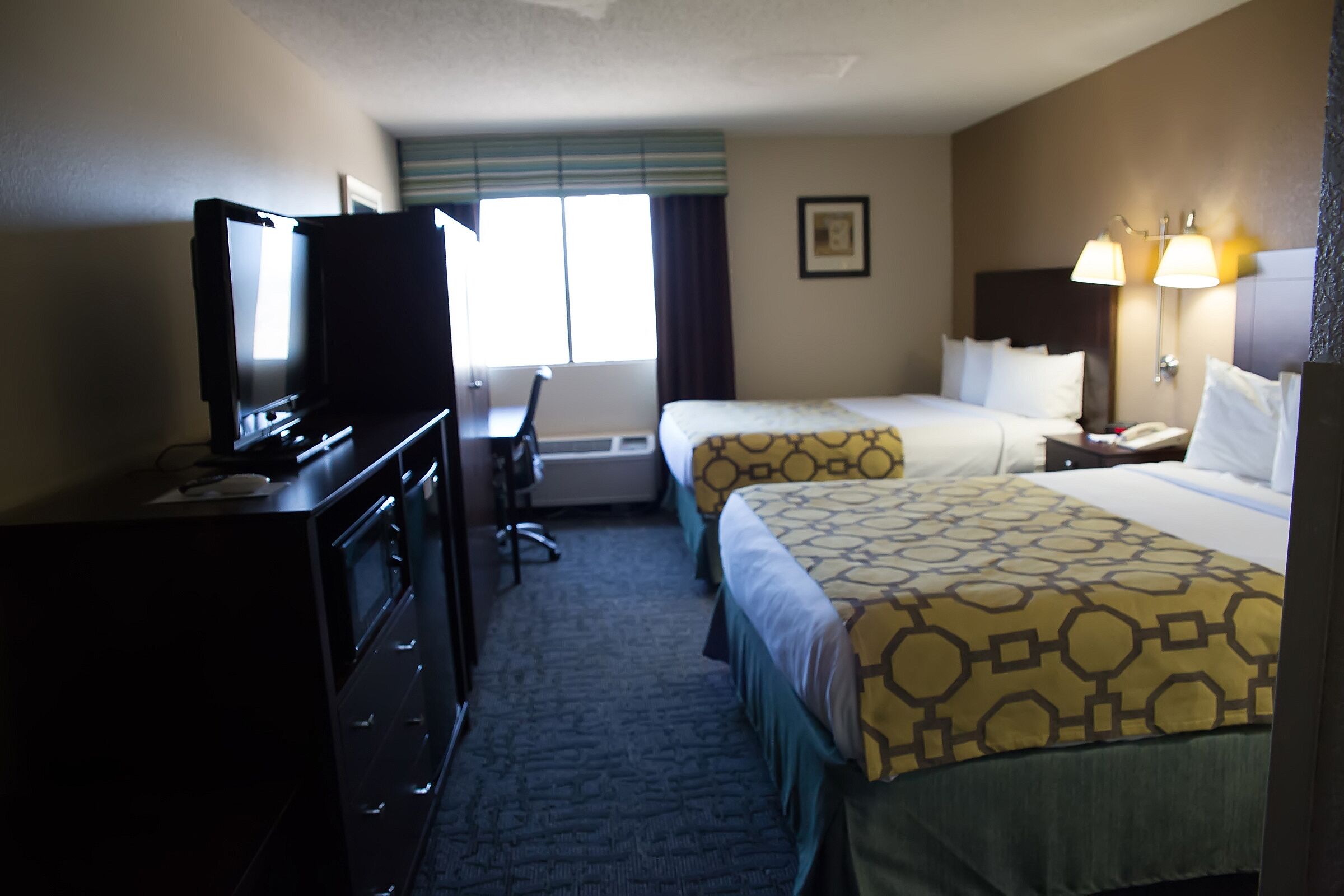 A hotel room with two beds, a desk, a television, and a window with curtains.