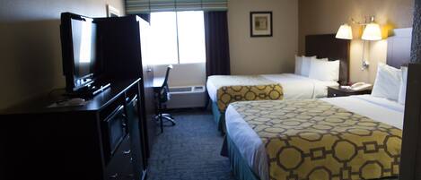 A hotel room with two beds, a desk, a television, and a window with curtains.