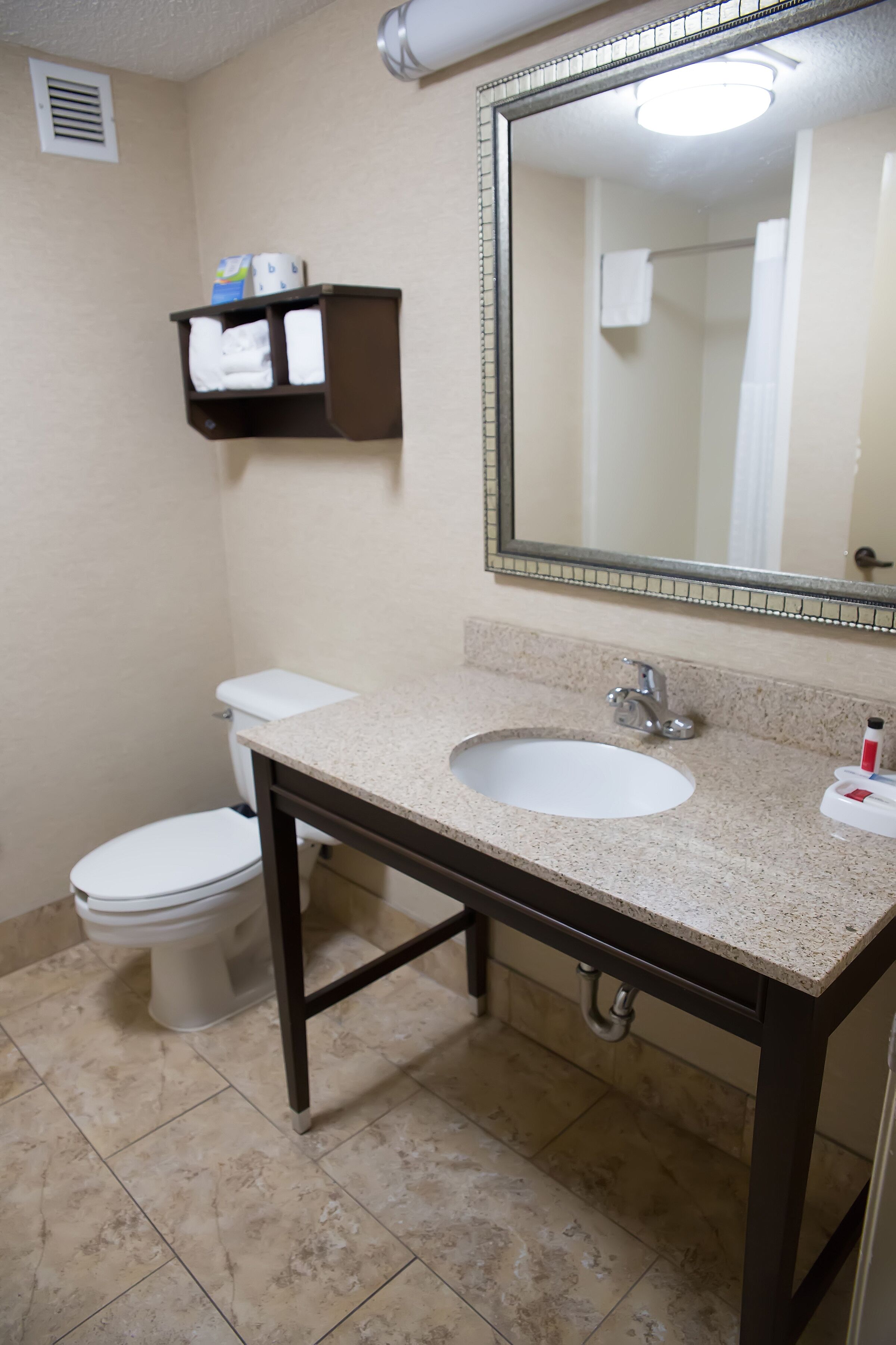 A bathroom with a white sink, a mirror, a toilet, and a shelf with towels.