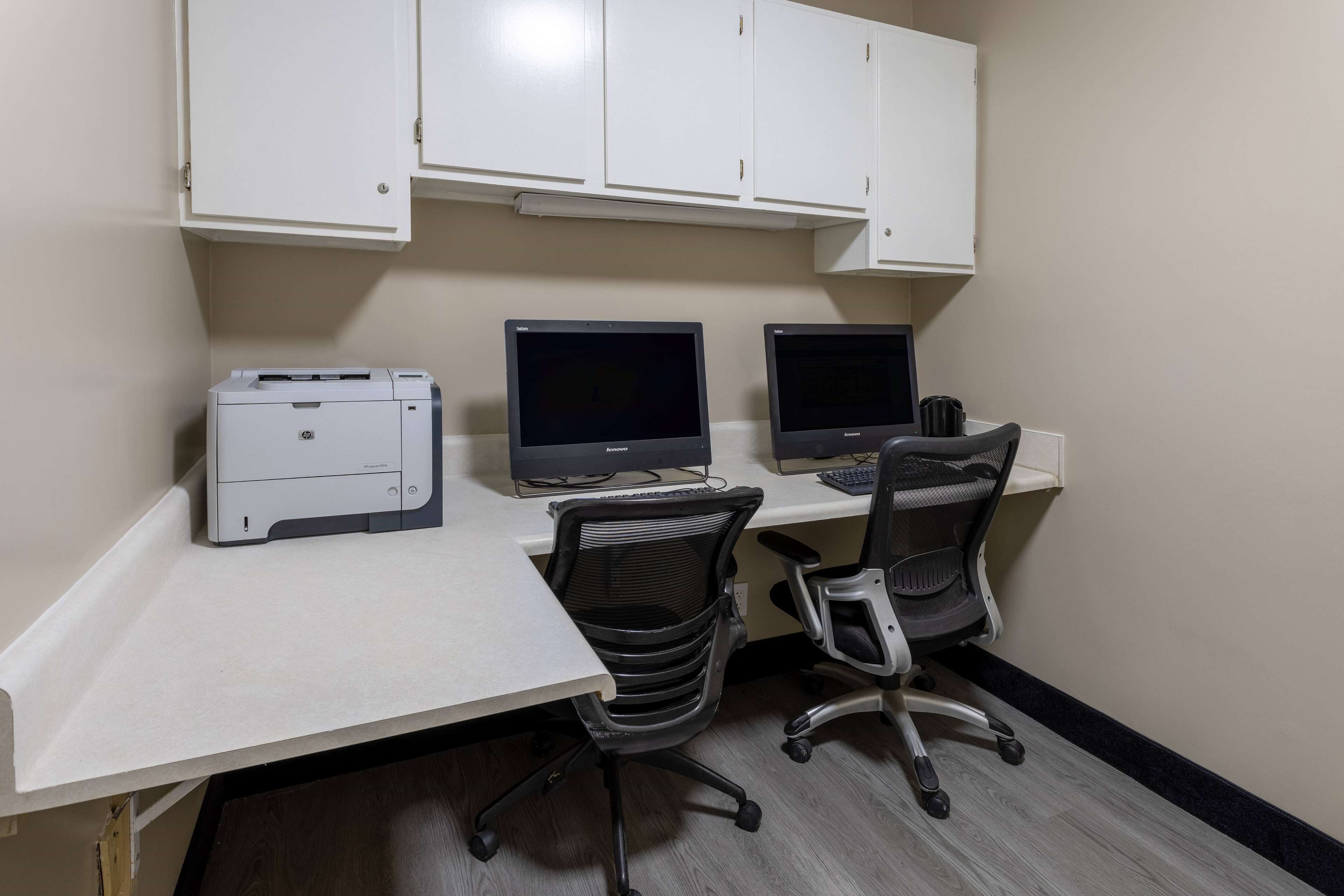 A workspace with two monitors, a printer, and two office chairs.