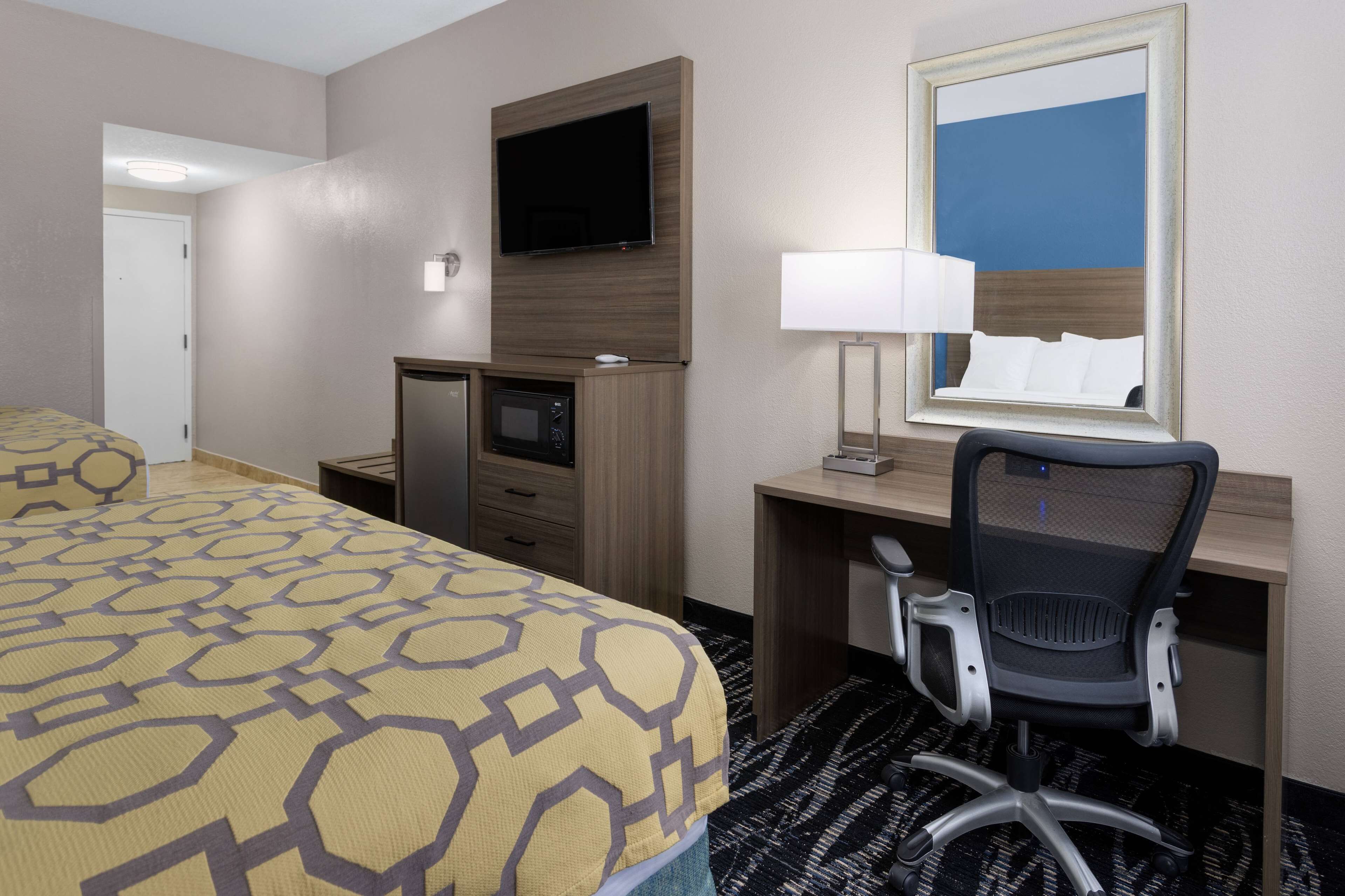 A hotel room with a bed, desk, chair, TV, and a mirror.