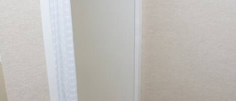 A bathroom with a glass shower enclosure, a white towel hanging on the shower rod, and beige tiled flooring.