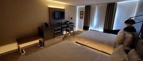 A hotel room with a bed, a desk with a chair, a television, and a window with curtains.