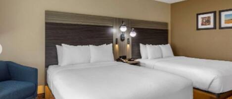 Habitación de hotel con dos camas, un sillón azul, cabecera con luces fijadas a la pared y cuadros enmarcados.