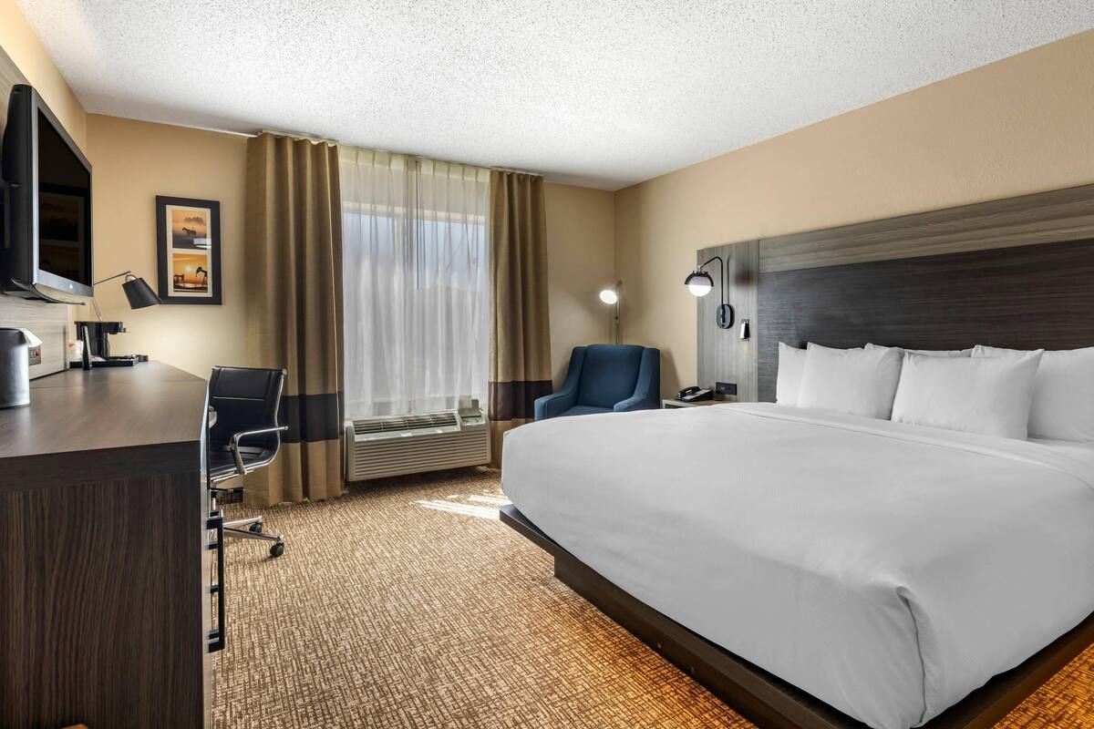Hotelkamer met een groot bed, een bureau met een computer, een stoel, een televisie en een raam met gordijnen.