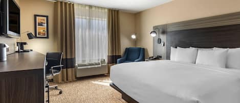 Ein Hotelzimmer mit einem großen Bett, einem Schreibtisch mit Computer, einem Sessel, einem Fernseher und einem Fenster mit Vorhängen.