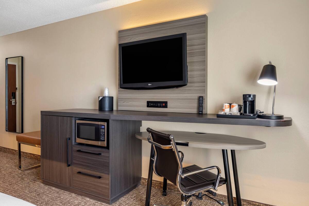 Een hotelkamer met een kitchenette, een flatscreen televisie aan de muur, een klein tafeltje met een stoel en een koffiezetapparaat.