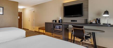 Habitación de hotel con dos camas, un escritorio, un televisor de pantalla plana, un microondas, una cafetera y una silla.