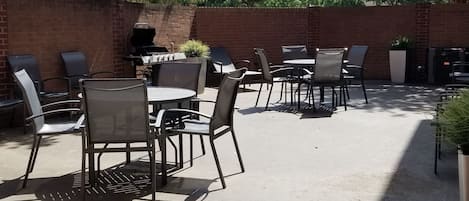 An outdoor patio with metal chairs and tables, a brick wall, and a grill.