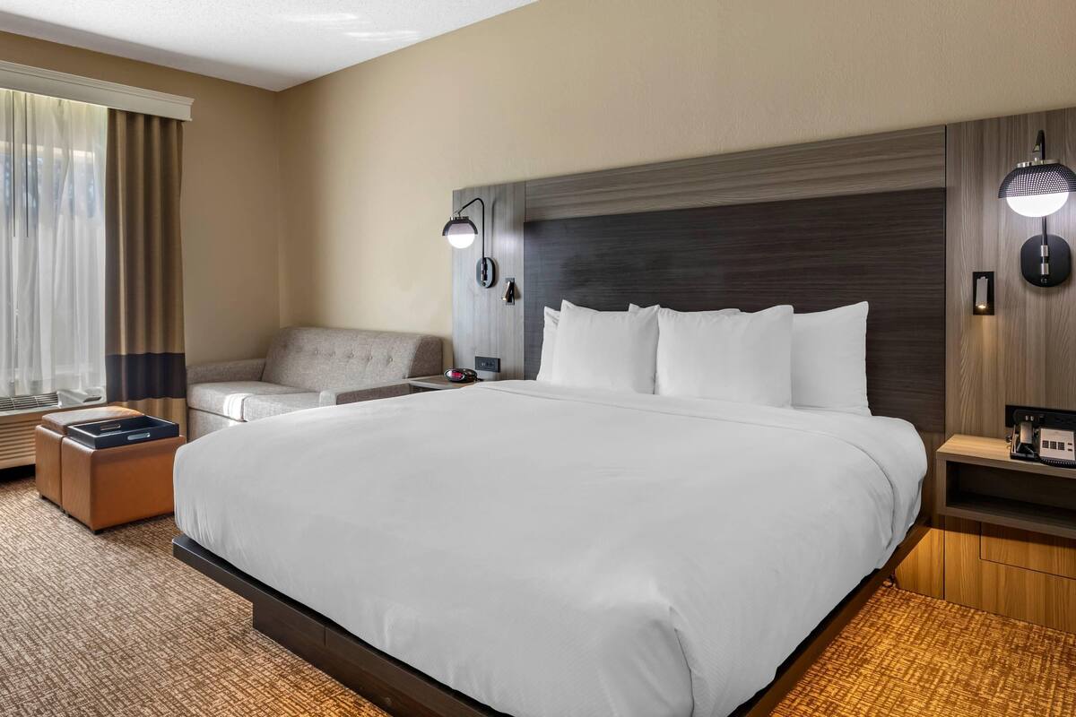 Hotelkamer met een groot bed, een slaapbank, een nachtkastje met een lamp en een raam met gordijnen.