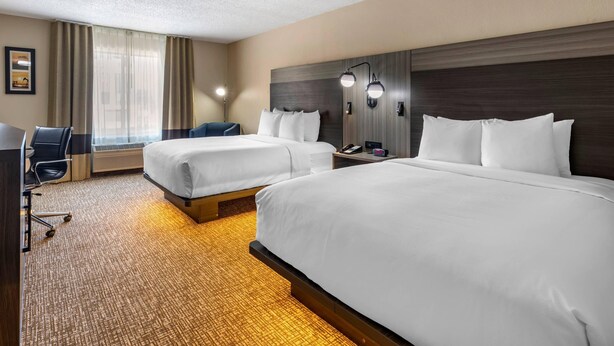 Een hotelkamer met twee bedden, een bureau, een stoel en een groot raam met gordijnen.