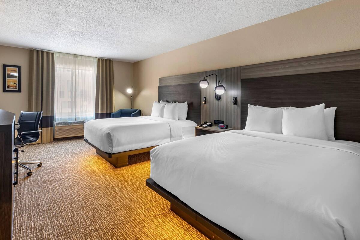 Een hotelkamer met twee bedden, een bureau, een stoel en een groot raam met gordijnen.