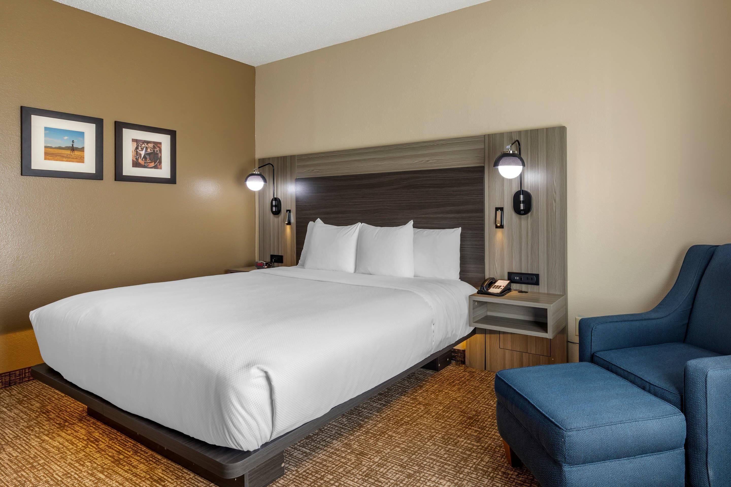 A hotel room with a large bed, a desk with a lamp, and a chair.