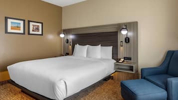 A hotel room with a large bed, a desk with a lamp, and a chair.