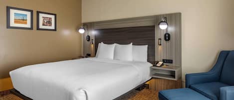 Una habitación de hotel con una cama grande, un escritorio con lámpara y una silla.