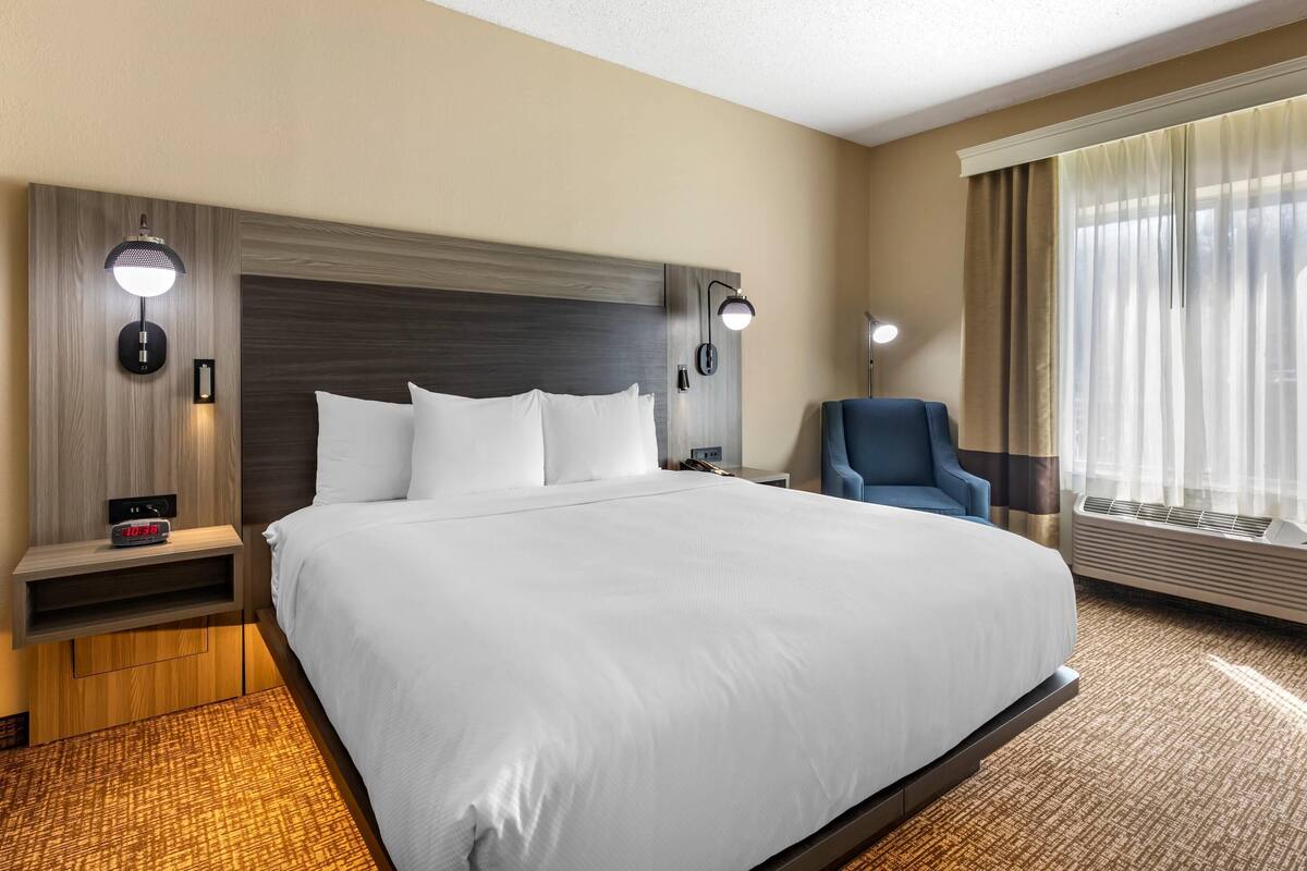 Een hotelkamer met een groot bed, nachtkastjes, een stoel en een raam met gordijnen.