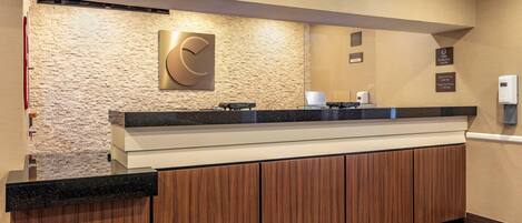A hotel reception area with a stone wall, a large 'C' logo, a check-in counter, and a smoke-free facility sign.