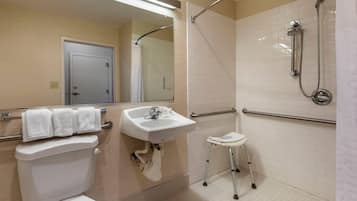 A bathroom with a toilet, sink, shower, and a small stool.